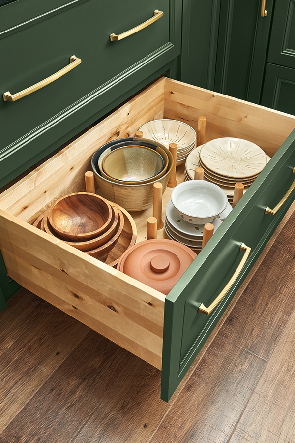Close-up of a pegged dish organizer inside a deep green Thomasville cabinet drawer, holding plates and bowls neatly in place for easy access.